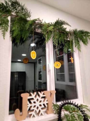 Window at night with winter greenery and dried orange slice garland hanging from the top.