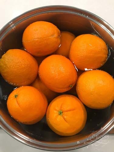 Whole oranges sitting in a vinegar/water bath in a metal bowl for two minutes.