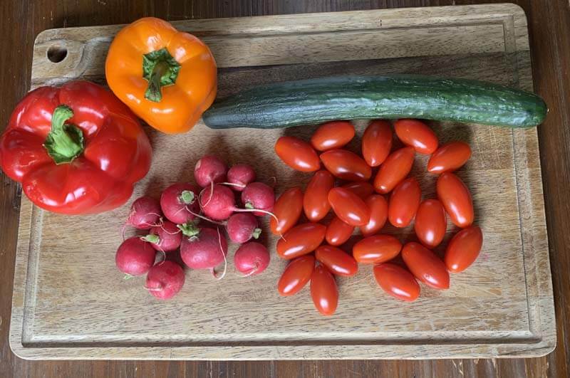 Wooden Cutting Board with bell peppers, cucumber, radish, and cherry tomatoes.