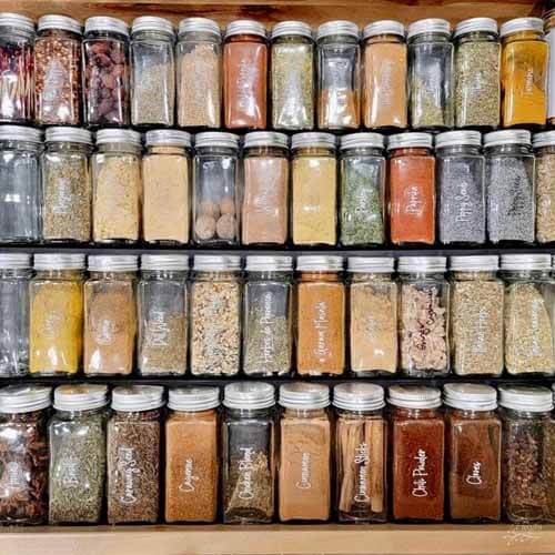 small glass jars that contain spices in kitchen spice drawer