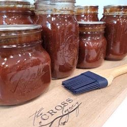 glass-jars-of-bbq-sauce-sitting-on-a-wooden-cutting-board-with-a-rubber-basting-brush