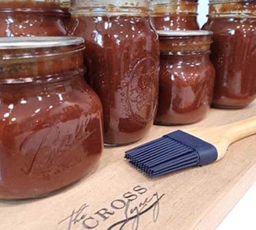 glass-jars-of-bbq-sauce-sitting-on-a-wooden-cutting-board-with-a-rubber-basting-brush