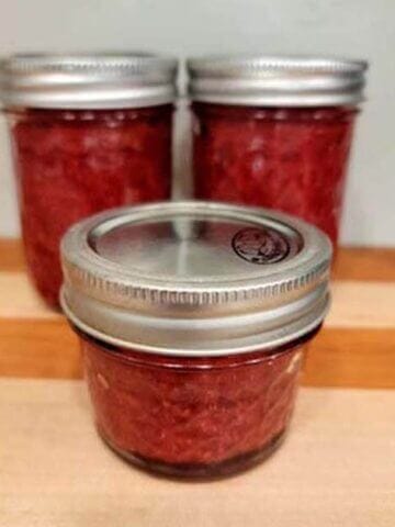 3 jars of homemade strawberry chia seed jam sitting on a wooden cutting board.