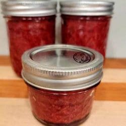 3 jars of homemade strawberry chia seed jam sitting on a wooden cutting board.