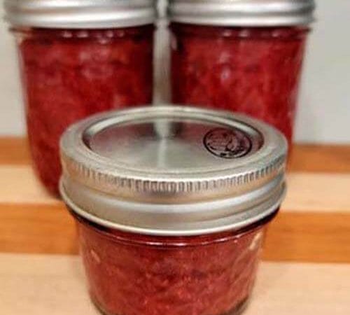 3 jars of homemade strawberry chia seed jam sitting on a wooden cutting board.