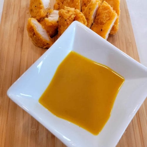 chopped-chicken-strips-on-a-wooden-cutting-board-with-honey-mustard-dressing-in-a-square-white-sauce-dishgydF4y2Ba