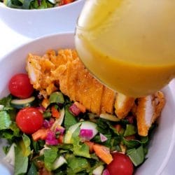 close-up-of-honey-mustard-salad-dressing-with-a-mixed-green-salad-with-chopped-chicken-stripsgydF4y2Ba