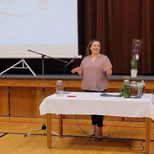 Amy Cross standing behind a table speaking at the Relief Society Women's Group.