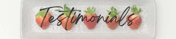 five fresh strawberries laying on a white rectangle serving tray with the word Testimonials across the graphic