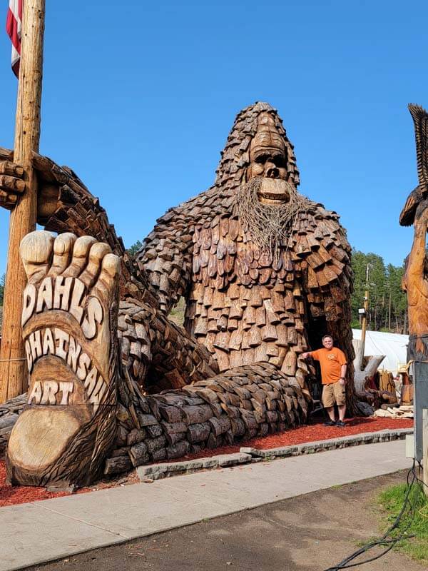 mike-cross-posing-with-Dahl's-chainsaw-art-of-the-biggest-bigfoot