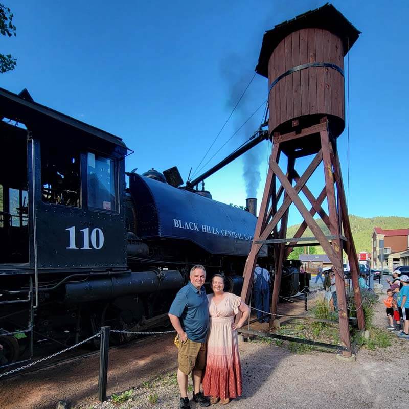 amy-and-mike-cross-posing-with-engine-110-of the-Black-Hills-1880-steam-train