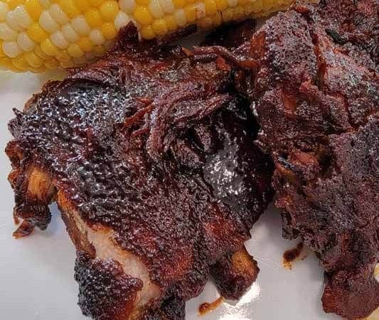 spare ribs with sweet and smokey rub and BBQ sauce and corn on the cob on a white plate