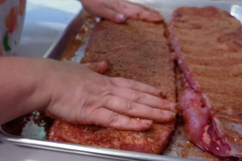 Amy Cross pressing her Sweet and Smoky Rib Rub onto a rack of ribs on a tray