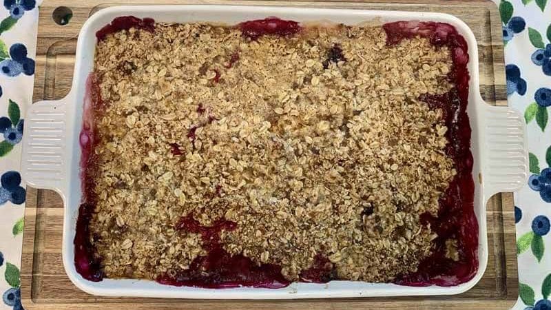fully cooked Peach Blueberry Crisp in a white baking dish cooling on a wooden cutting board
