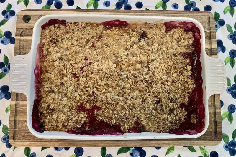 fully cooked Peach Blueberry Crisp in a white baking dish cooling on a wooden cutting board