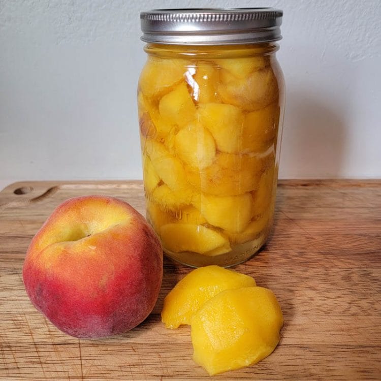新鲜的桃子和去皮的桃子，用于桃子罐头和一罐罐头桃子坐在一个木砧板上