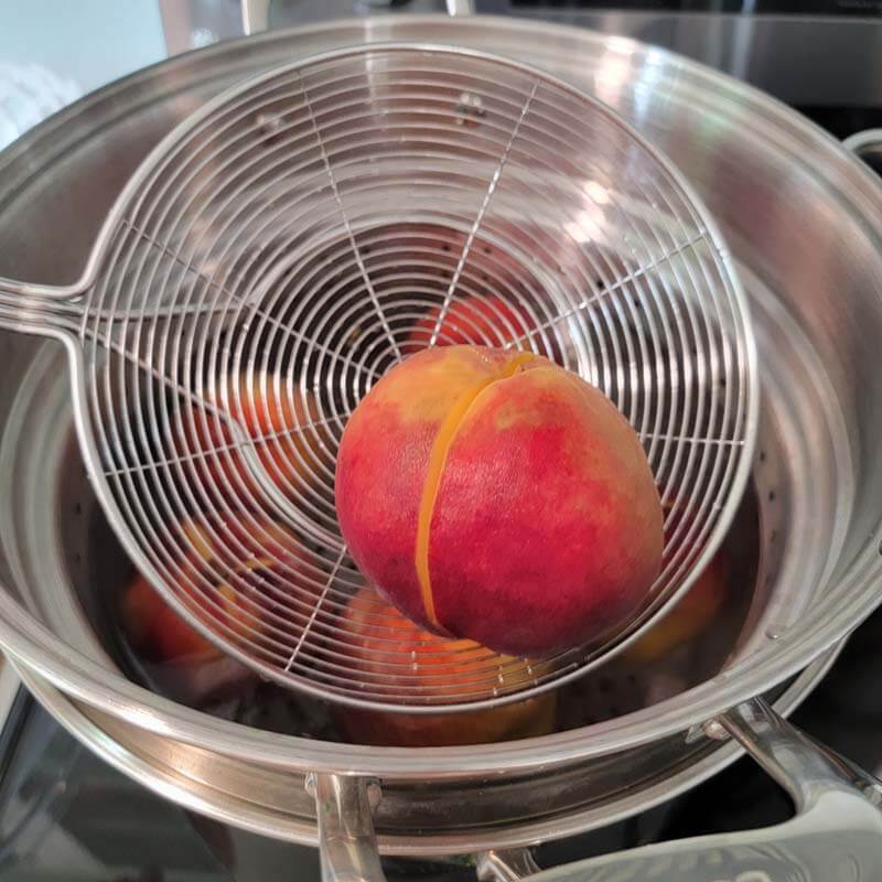 spider strainer with a blanched peach for water bath canning