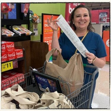 Amy at the grocery store with her grocery cart holding her receipt and smiling.