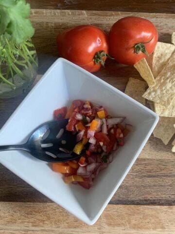fresh cilantro and tomatoes with corn chips and salsa in a white bowl