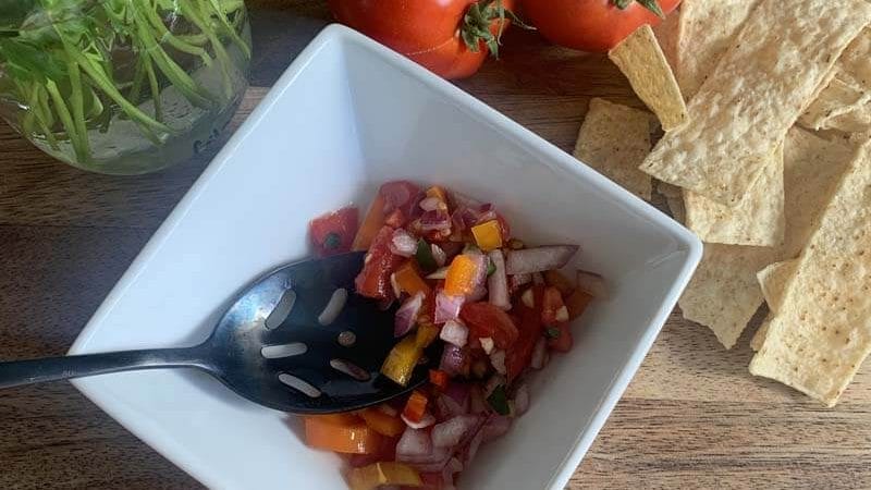 fresh cilantro and tomatoes with corn chips and salsa in a white bowl