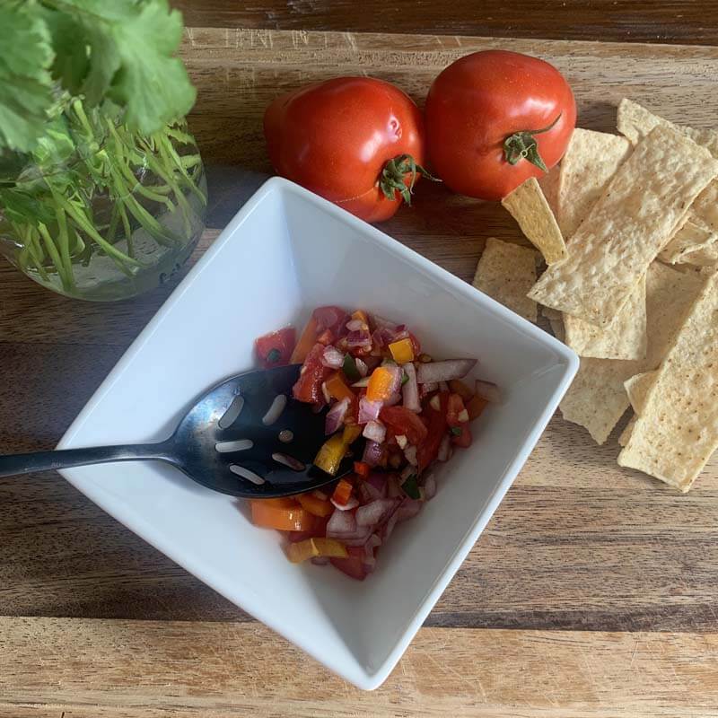 fresh cilantro and tomatoes with corn chips and salsa in a white bowl