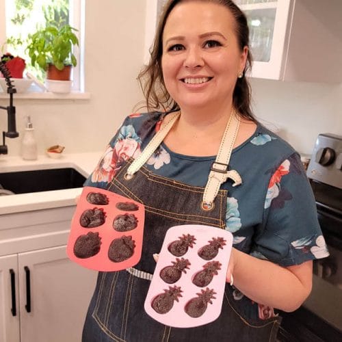 艾米·克罗斯站在厨房里，手里拿着自制的接骨木软糖，装在菠萝和草莓的硅胶模具里gydF4y2Ba