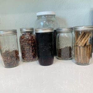 Anise, rosehips, whole cloves, elderberries, ceylon cinnamon sticks, in glass jars sitting on the counter