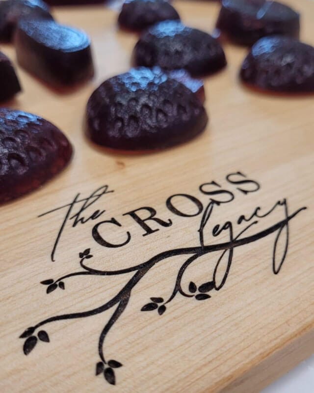 close up of strawberry shaped elderberry gummies sitting on a wooden cutting board with The Cross Legacy logo engraved on it