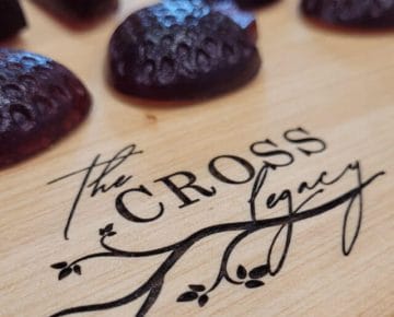 close up of strawberry shaped elderberry gummies sitting on a wooden cutting board with The Cross Legacy logo engraved on it