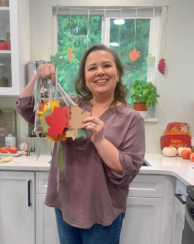 Amy in her kitchen holding keepsakes to cherish written on paper leaves over the years.