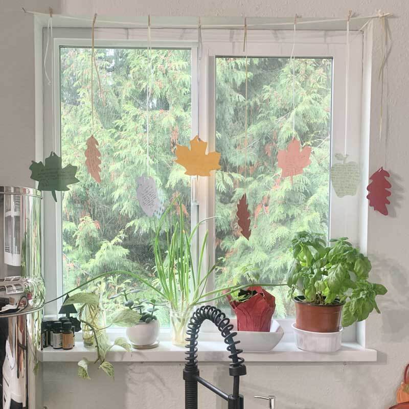 Paper fall leaves hanging from string in kitchen window with sentimental notes written on them.