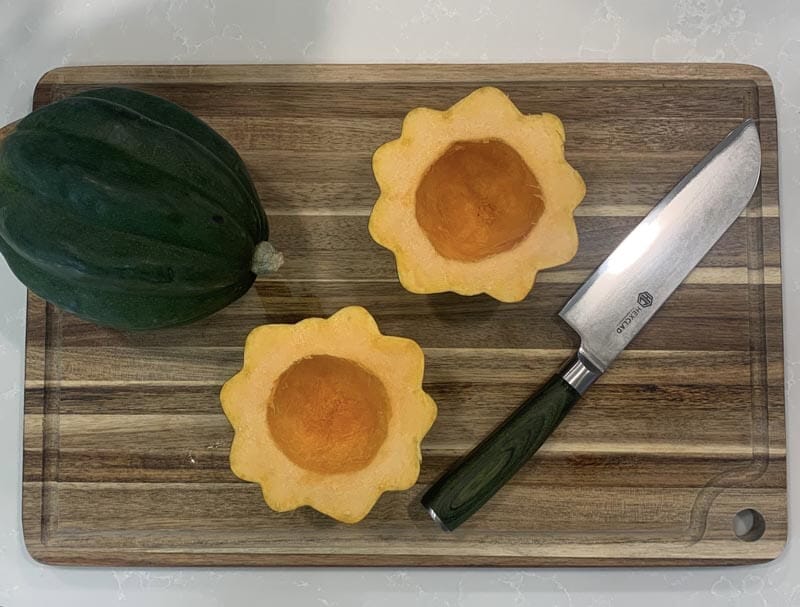 One whole acorn squash and one cut in half on a cutting board with a knife.