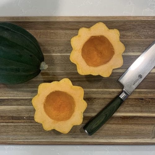 One whole acorn squash and one cut in half on a cutting board with a knife.