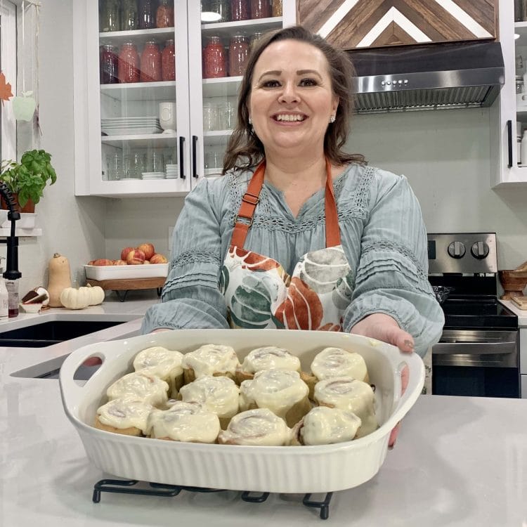 Amy holding a dish of her finished Christmas Morning Cinnamon Rolls in her kitchen.