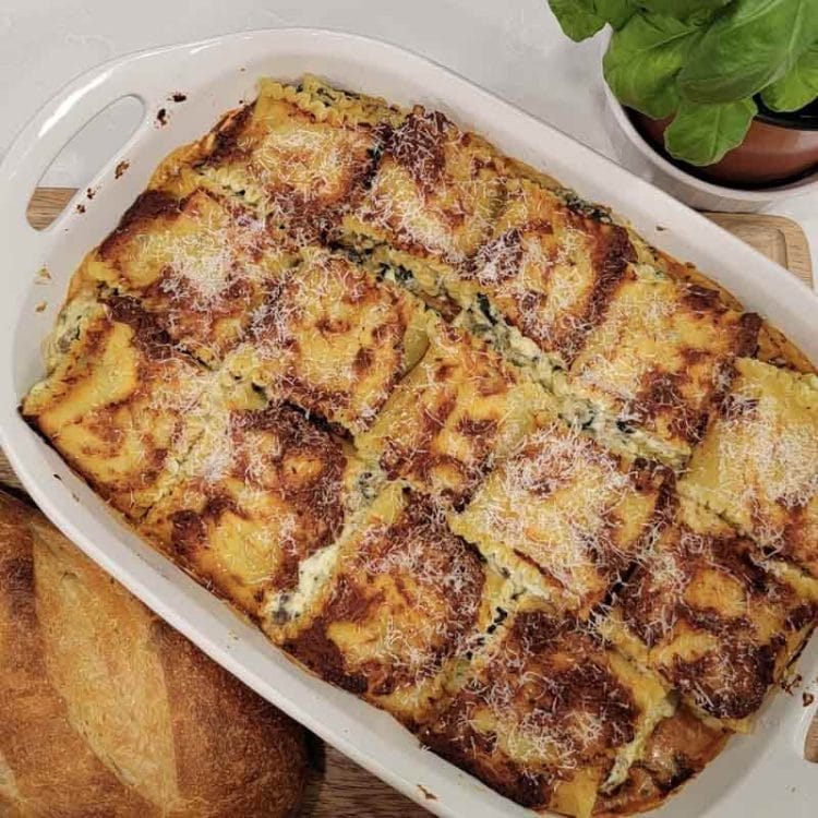 Baked Lasagna Rolls in white casserole dish with a loaf of crusty bread and basil plant.