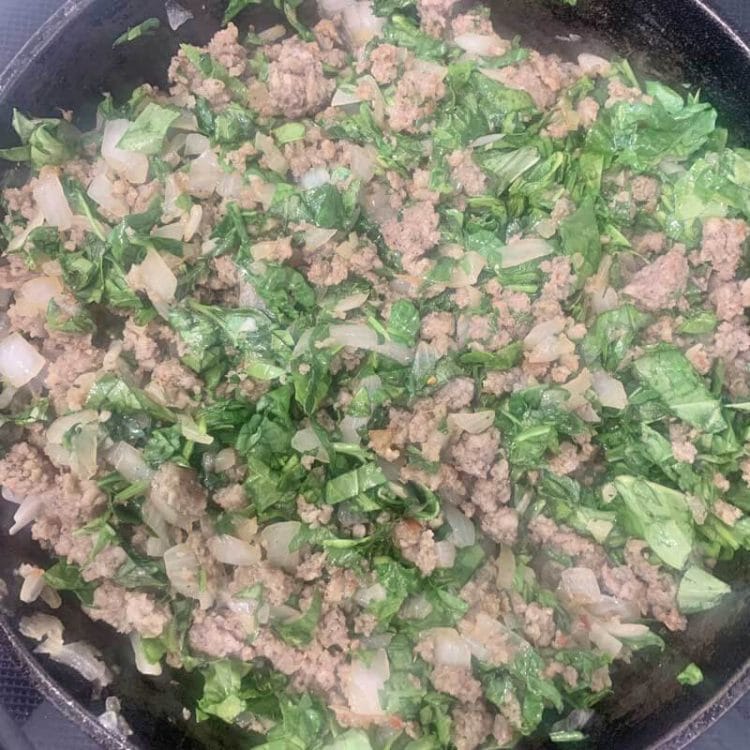 Sausage, chopped spinach, and onion in a pan.
