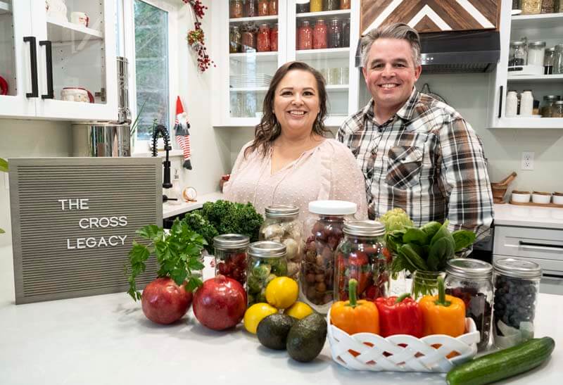 Amy and Mike Cross in their kitchen with a spread of fresh produce and The Cross Legacy sign.