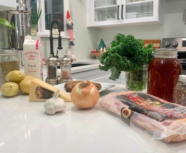 All Simple Ingredients it takes to make Zuppa Toscana - potatoes, parmesan cheese, garlic, onion, heavy cream, bacon, kale, stock, etc. laid out on the counter.