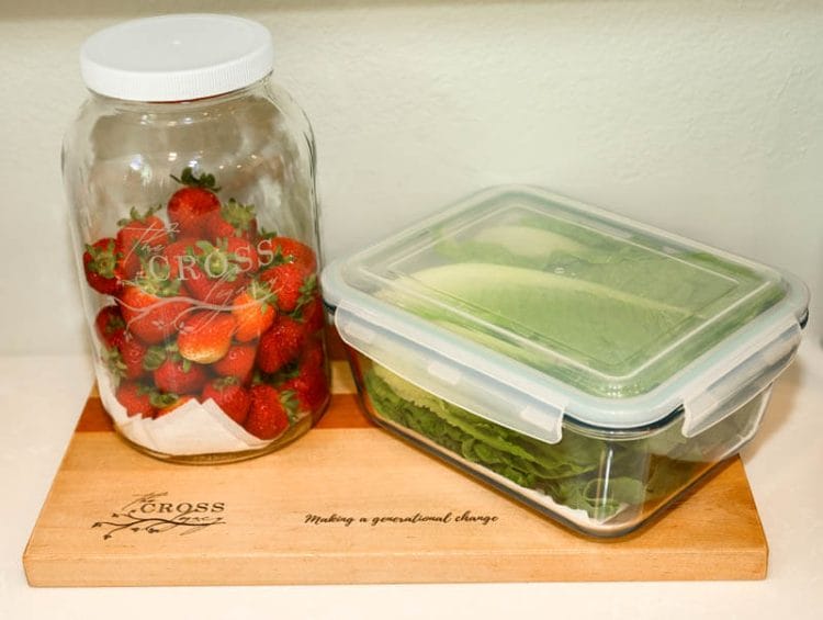 Fresh strawberries and romaine lettuce in glass jars sitting on a wooden cutting board.