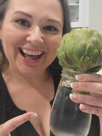 Amy Cross holding a glass mason jar filled with water and a fresh artichoke.
