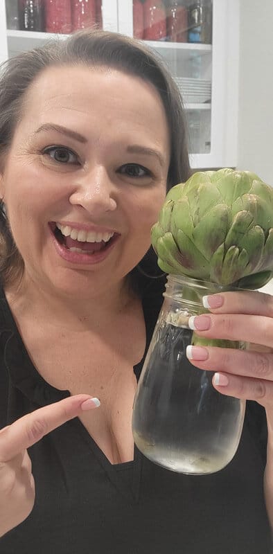 Amy Cross holding a glass mason jar filled with water and a fresh artichoke.