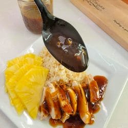 White plate with fresh sliced pineapple, brown rice, and chicken with homemade teriyaki sauce.