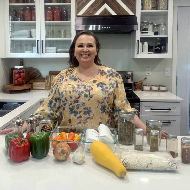 Amy Cross standing at her kitchen counter with all the ingredients needed to make her Homemade Taco Seasoning and batch cooked taco meat recipes.