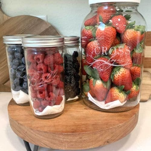新鲜浆果——草莓、覆盆子、黑莓和蓝莓装在柜台上的玻璃瓶里。