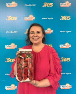 Amy Cross in front of the New Day Northwest / King 5 background holding her strawberries in a jar.