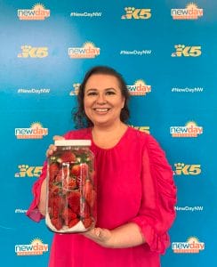Amy Cross在New Day Northwest / King 5背景前拿着她的草莓在一个罐子里。