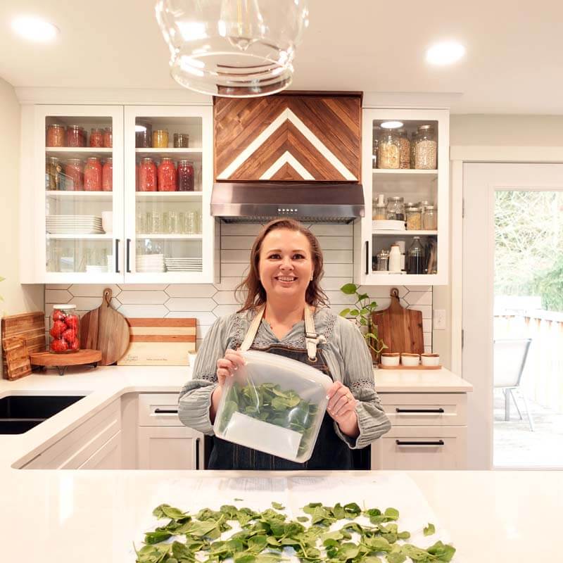Amy standing at her kitchen counter holding a Stasher bag of spinach, which is her favorite ay to store spinach in the freezer for smoothies.