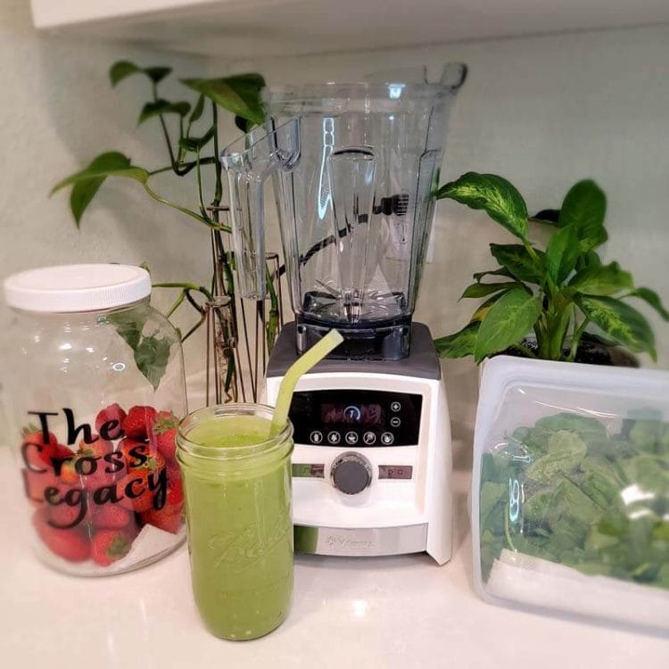 Blender, Green Smoothie, Stasher bag of spinach and a jar of strawberries on the counter.
