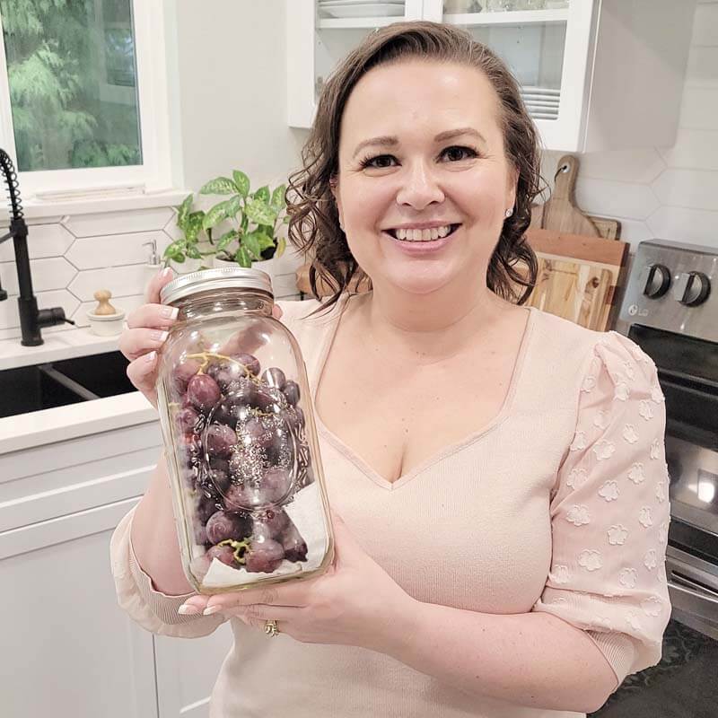 Amy Cross in her kitchen holding fresh grapes in a glass airtight container.