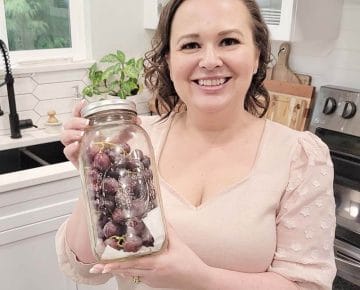 Amy Cross in her kitchen holding fresh grapes in a glass airtight container.